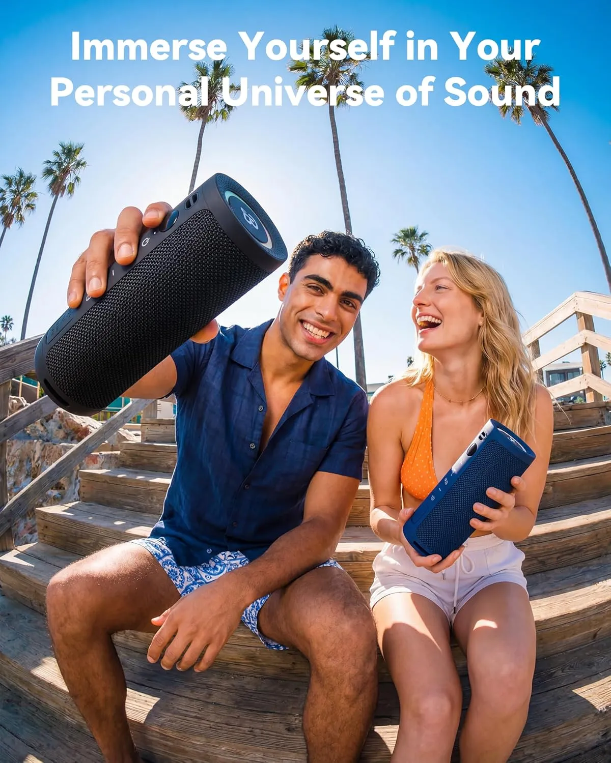 Two people outdoors among palm trees with black and blue BassBloom Roar 3 speakers