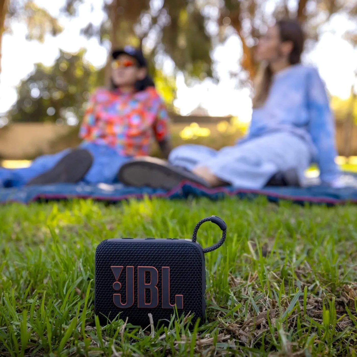 JBL Go 4 outdoor lifestyle: portable speaker on grass during a picnic with friends
