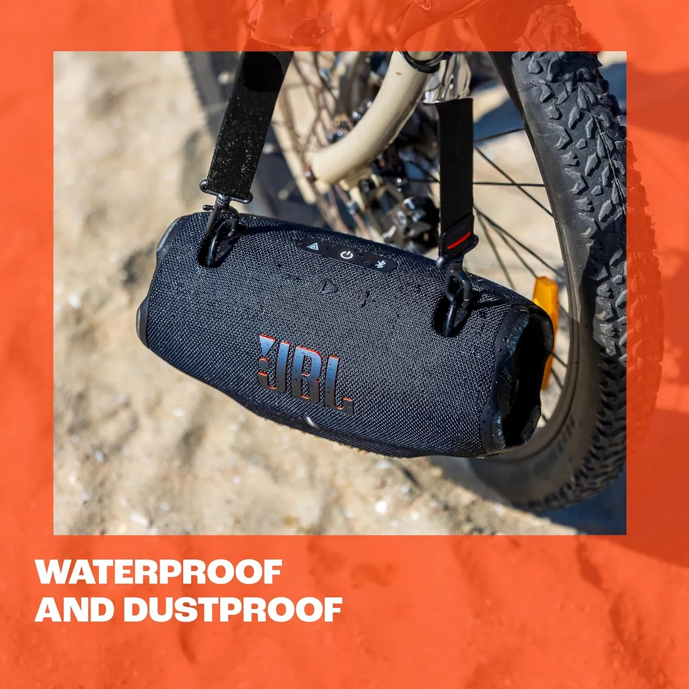 JBL Xtreme 4 hanging from a bicycle handlebar on sand, illustrating the IP67 waterproof and dustproof rating