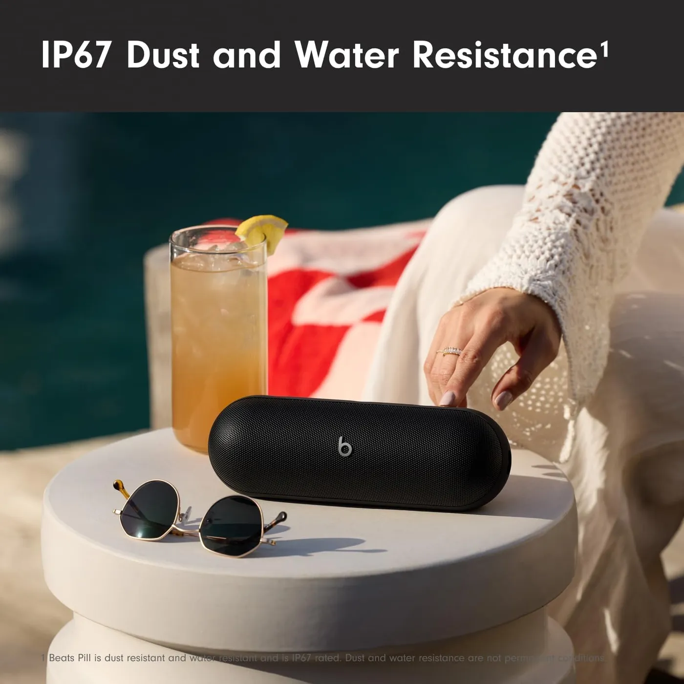 Beats Pill (2024) Bluetooth speaker poolside beside a drink, showing IP67 dust and water resistance