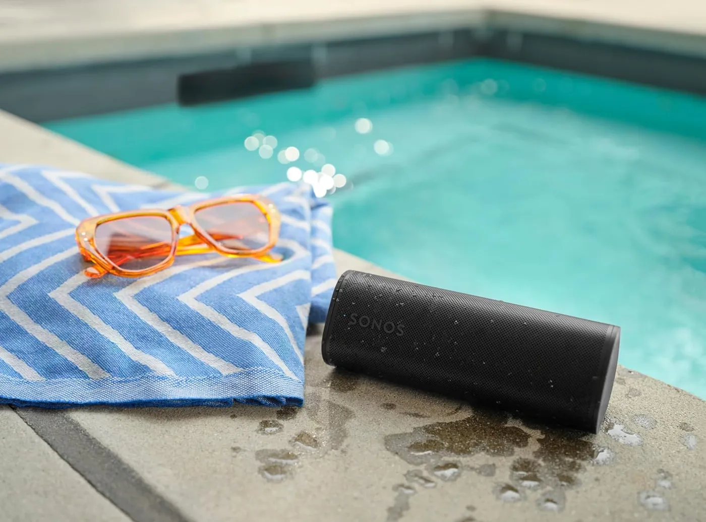 Sonos Roam 2 waterproof speaker beside a swimming pool with a towel and sunglasses