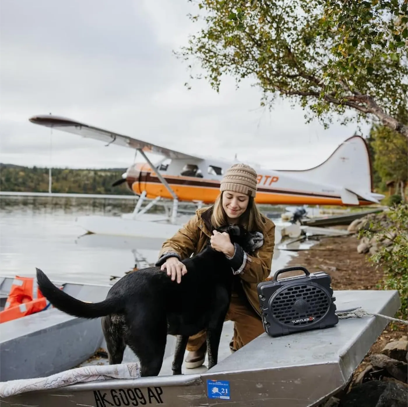 Woman and dog on a boat beside a seaplane with the Turtlebox Original Gen 3 Bluetooth speaker
