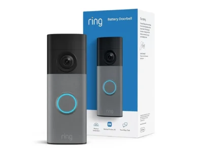 Ring Battery Doorbell 2K in Speckled Gray with its glowing blue button ring, standing in front of the retail box