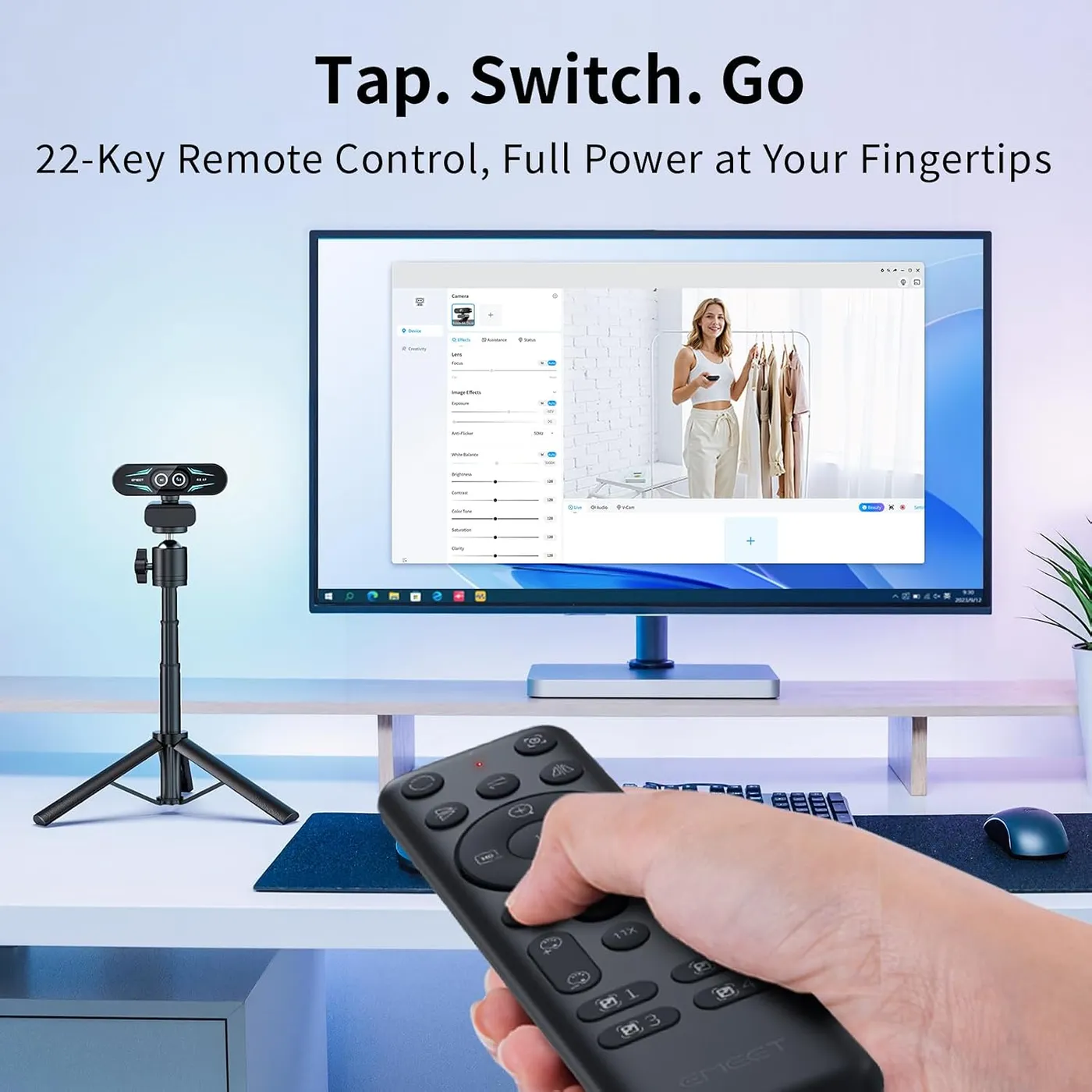 EMEET C60E Dual-Camera 4K Webcam on a small tripod beside a monitor, a hand holding its 22-key remote in the foreground